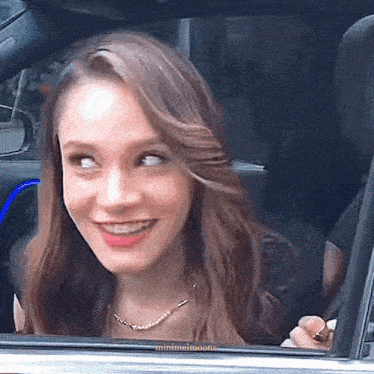 a woman is smiling while looking out of a car window .