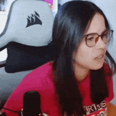 a woman wearing glasses and a red shirt is sitting in front of a corsair chair .