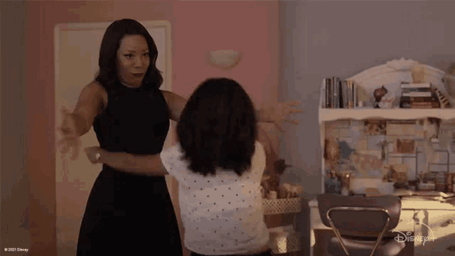 a woman in a black dress is hugging a little girl in front of a disney+ desk