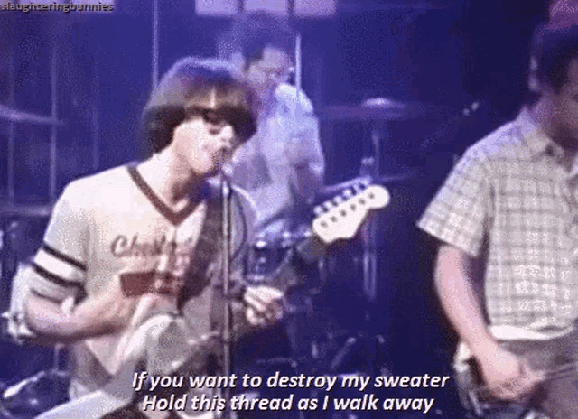 a man singing into a microphone while playing a guitar with the words if you want to destroy my sweater