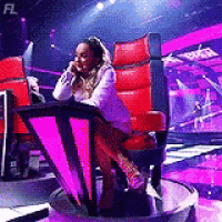 a woman is sitting in a red chair on a stage talking on a phone .
