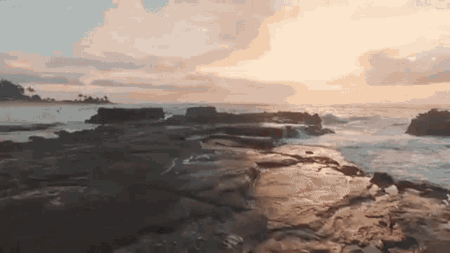 a sunset over the ocean with rocks in the foreground and waves crashing on the shore .