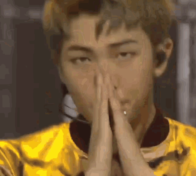 a close up of a man wearing a yellow jacket with his hands folded in front of his face .