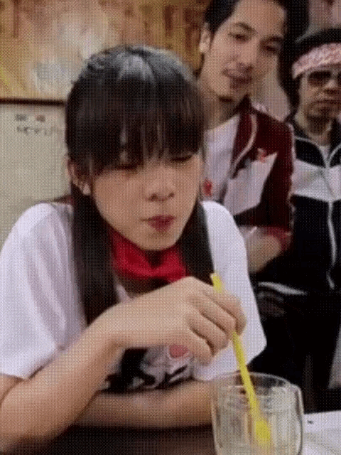 a girl sitting at a table with a straw in her hand