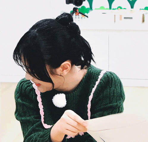 a woman wearing a green sweater with a white pom pom on the collar