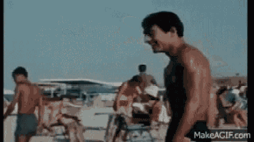 a man without a shirt is standing on a beach with other people .