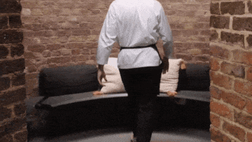 a man in a white shirt and black pants is walking towards a brick wall