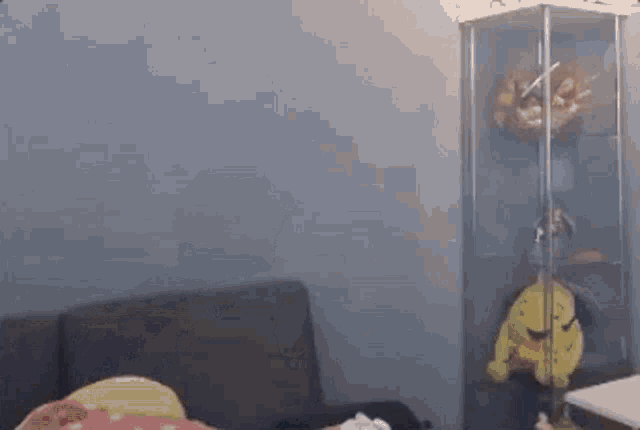 a person is sitting on a couch in a living room next to a glass case with stuffed animals on it .