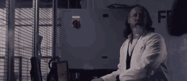 a man in a lab coat is sitting at a desk in a room .