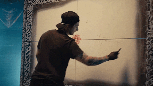 a man wearing a black hat and a black shirt is painting on a wall