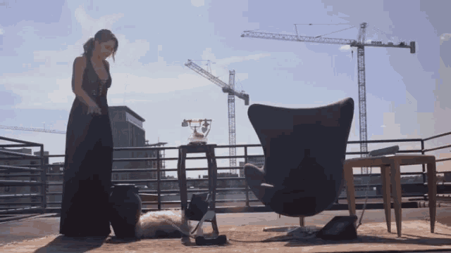 a woman in a black dress stands in front of a chair