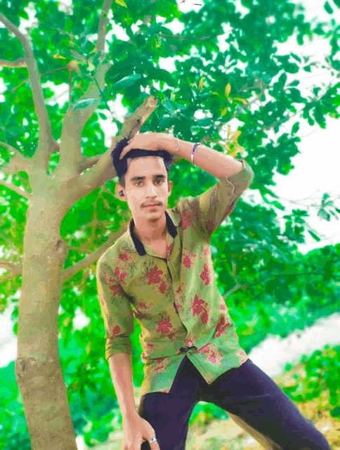 a young man in a green floral shirt is sitting under a tree