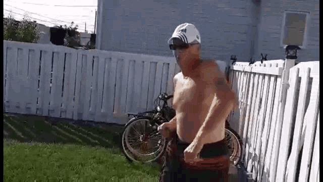 a shirtless man is running in front of a white fence with bicycles in the background .