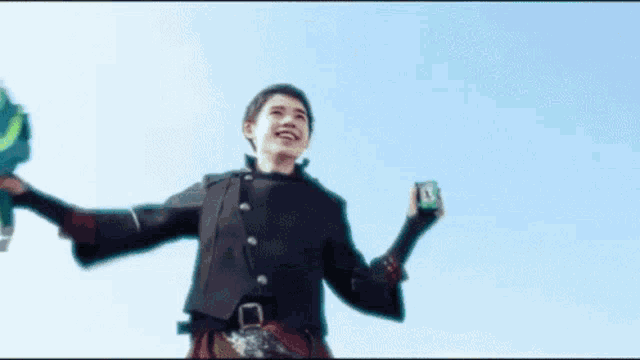 a man in a black jacket is holding a green object in his hand and laughing .