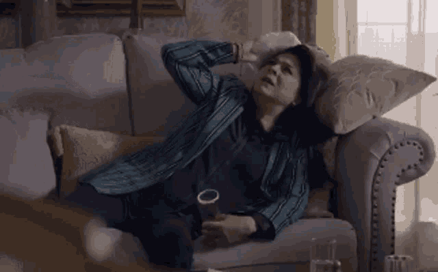 a woman is laying on a couch holding a glass of beer .