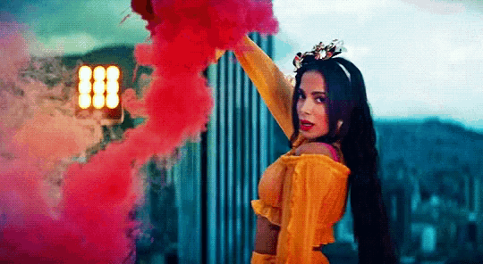 a woman in a yellow dress is holding a smoke bomb in her hand .