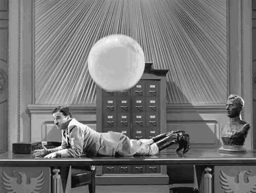 a black and white photo of a man laying on his stomach with a ball floating in the air