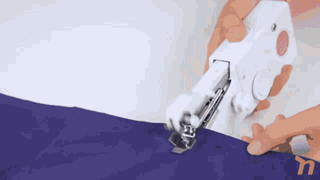 a person is using a portable sewing machine to sew a piece of fabric .