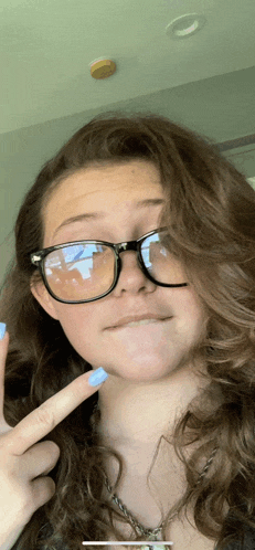 a woman wearing glasses and blue nail polish is making a face