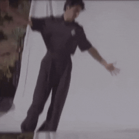 a man in a black jumpsuit is dancing in front of a white curtain