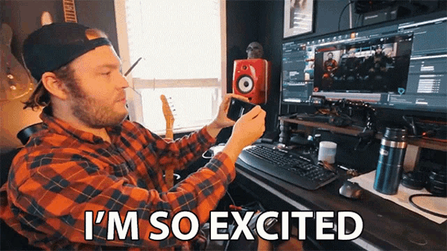 a man in a plaid shirt is sitting in front of a computer with the words i 'm so excited above him