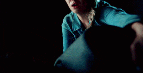 a woman in a blue shirt is sitting in a dark room holding a pillow .