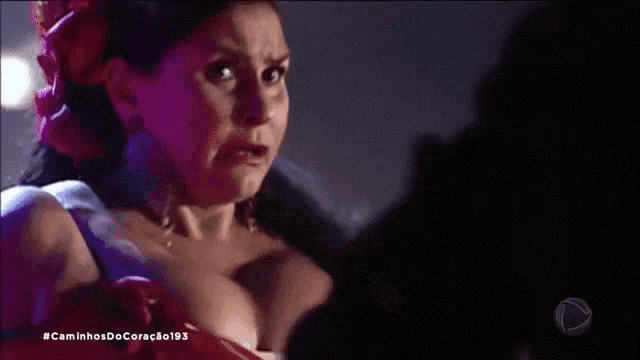 a woman in a red dress with a flower in her hair is standing in the dark .