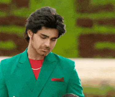 a man wearing a green jacket and a red shirt looks down