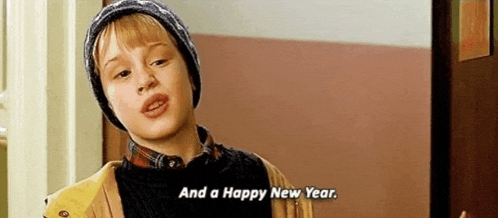 a young boy wearing a beanie is standing in front of a door and saying `` and a happy new year '' .