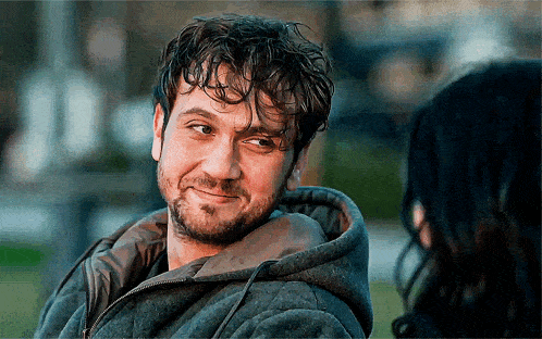 a man with a beard wearing a hoodie looks at a woman