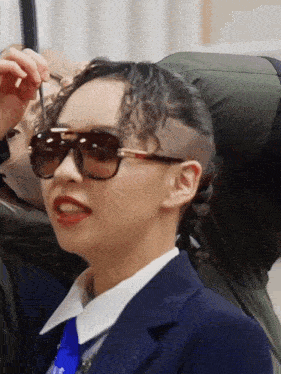a woman with a shaved head wears sunglasses and a suit