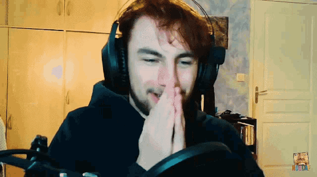 a man wearing headphones prays in front of a microphone with a rainbow logo in the corner
