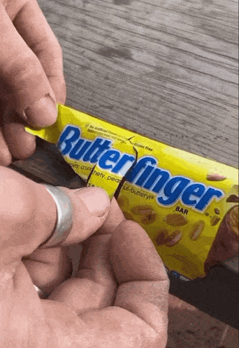 a person is opening a butterfinger bar with a ring on their finger