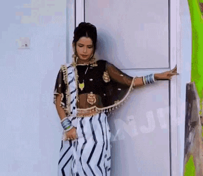 a woman in a white and black striped saree is standing in front of a door .