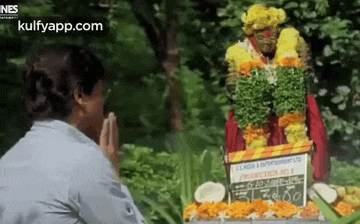 a man is praying in front of a statue of a woman with flowers around her head .