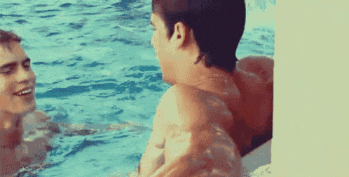 two men are talking in a swimming pool without shirts .