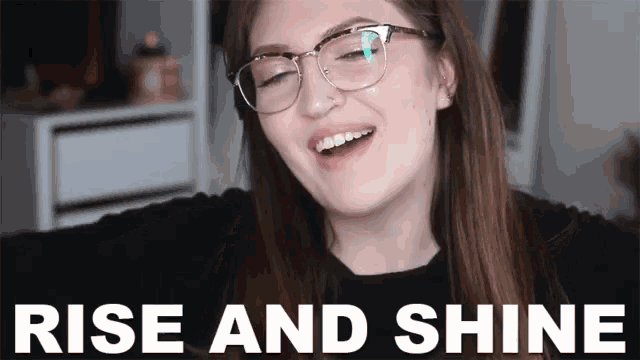 a woman wearing glasses is smiling in front of a sign that says rise and shine