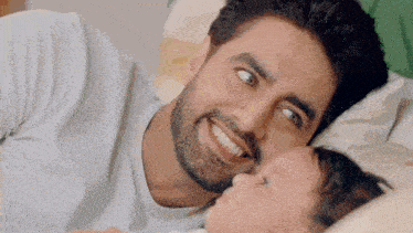 a man is laying in bed with a baby and smiling .