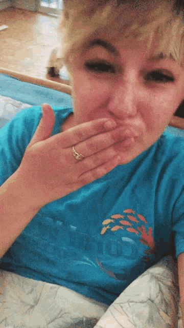a woman wearing a blue shirt with a fish on it covers her mouth with her hand