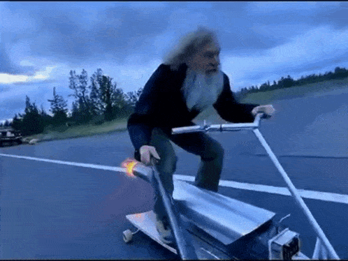 an older man with a beard is riding a skateboard on a road .