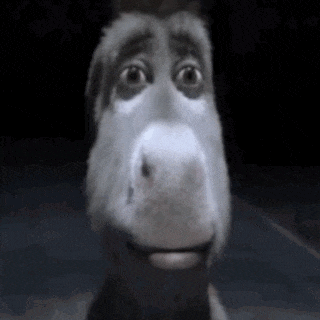 a donkey from the movie shrek is smiling and looking at the camera in the dark .