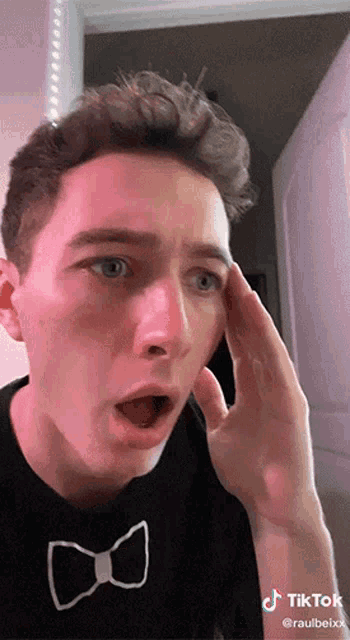 a young man wearing a black shirt with a white bow tie has a tiktok on his face