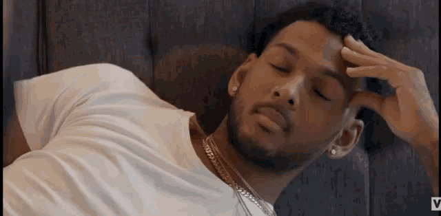 a man in a white shirt is laying on a couch with his hand on his forehead