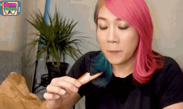 a woman with pink and blue hair is eating a piece of food while watching some show tv