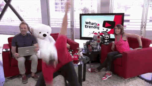 a man is holding a teddy bear in front of a tv screen that says what 's trending