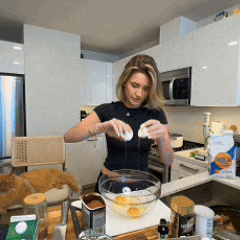 a woman in a black shirt is cracking eggs into a bowl in a kitchen