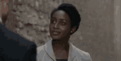 a priest is smiling while talking to a woman in front of a brick wall .