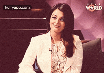 a woman in a white jacket is sitting on a couch with a star world logo in the background .