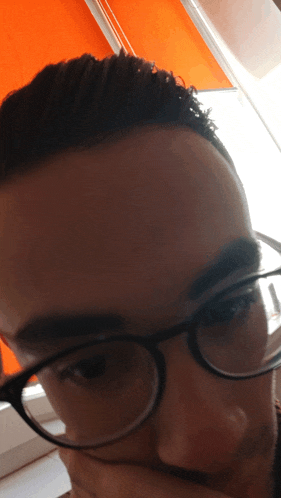 a man wearing glasses looks at the camera with his hand on his chin