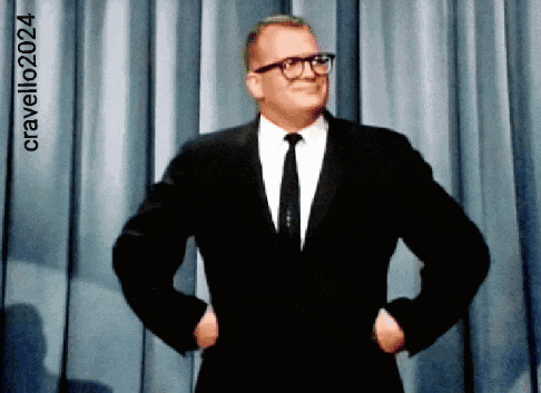 a man in a suit and tie stands with his hands on his hips in front of a blue curtain with cravello2024 written on it
